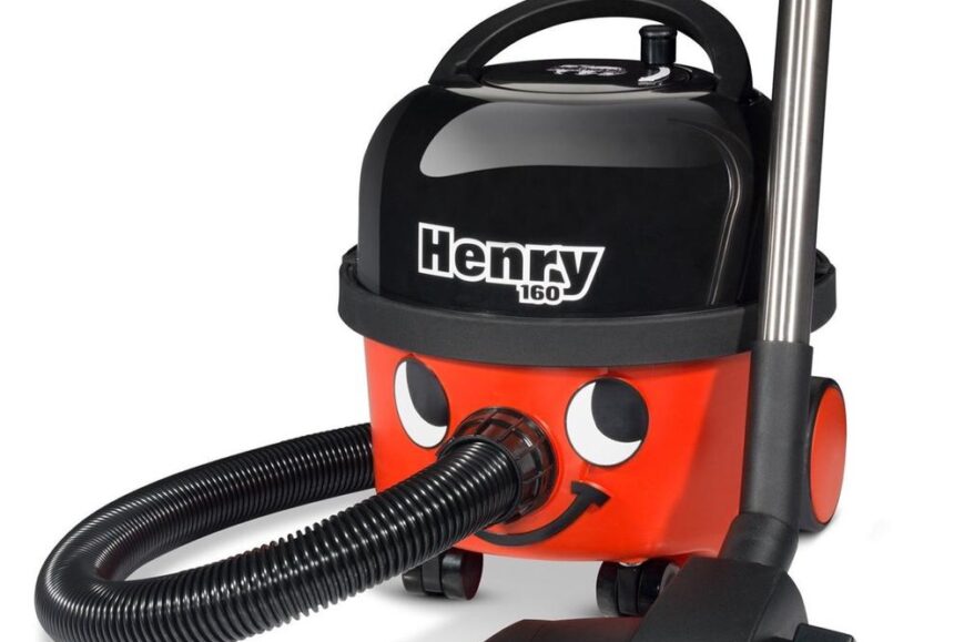 Een vrolijke stofzuiger met een lachend gezicht, genaamd Henry 160, met een zwarte bovenkant en een opvallende rode onderkant. De stofzuiger heeft een flexibele slang en een stevige zuigmond op een vlak oppervlak geplaatst.
