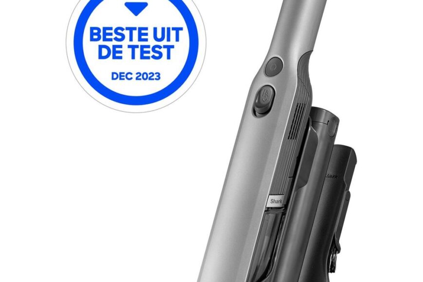 Een zilverkleurige handstofzuiger van het merk Shark, geplaatst in een laadstation. Boven de stofzuiger bevindt zich een label van de Consumentenbond met de tekst "Beste uit de test" en de datum "dec 2023".