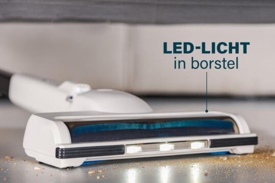 Afbeelding van een handstofzuiger met een borstelsysteem dat is uitgerust met een LED-lampje, dat helpt om stof en vuil beter zichtbaar te maken tijdens het schoonmaken. De onderkant van de stofzuiger ligt naast een vuilige ondergrond, waar kleine deeltjes zichtbaar zijn.