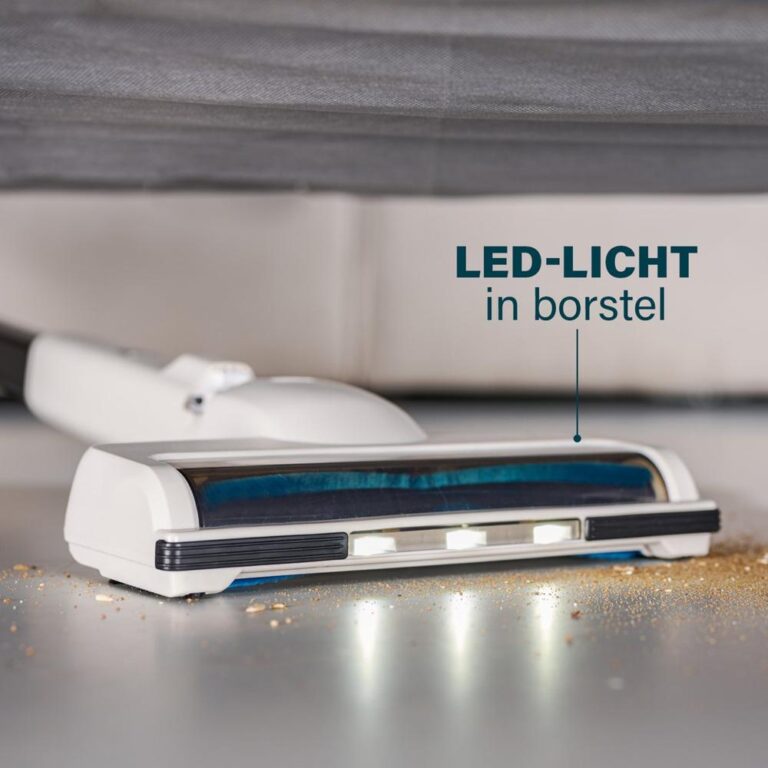 Afbeelding van een handstofzuiger met een borstelsysteem dat is uitgerust met een LED-lampje, dat helpt om stof en vuil beter zichtbaar te maken tijdens het schoonmaken. De onderkant van de stofzuiger ligt naast een vuilige ondergrond, waar kleine deeltjes zichtbaar zijn.