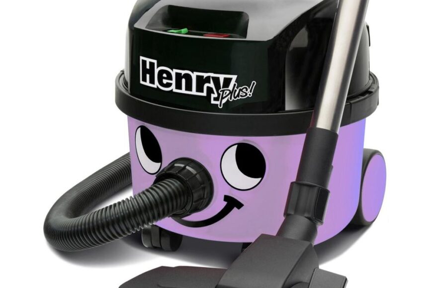 Een kleurrijke stofzuiger met een lachend gezicht, genaamd Henry Plus, die is uitgerust met een slang en een stofzuigmond. De stofzuiger is lila van kleur en heeft een zwart bovenste gedeelte met knoppen.