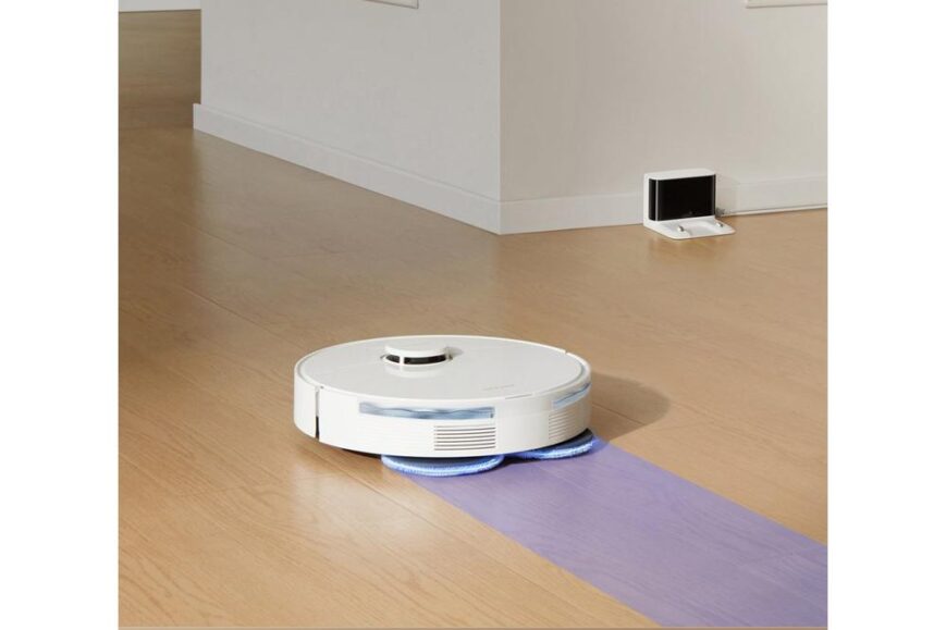 Robotstofzuiger op een houten vloer, uitgerust met twee draaiende dweilpads voor efficiënt schoonmaken. De afbeelding toont het apparaat in actie, terwijl het hardnekkig vuil en gemorste vloeistoffen verwijdert.
