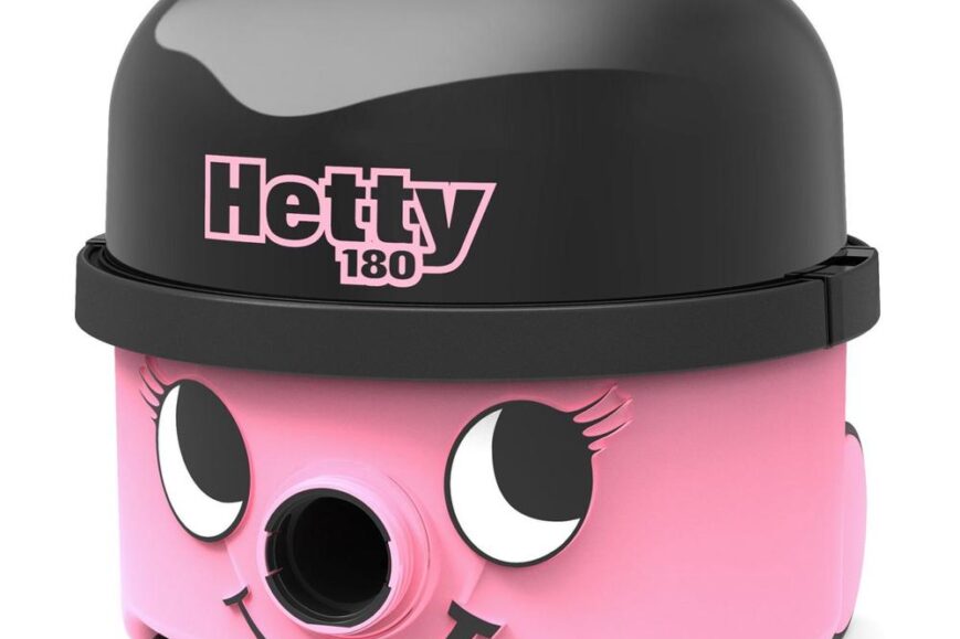 Een roze stofzuiger met een glimlachend gezicht en grote ogen, gemarkeerd met de naam "Hetty 180" op de bovenkant. De stofzuiger heeft een zwart bovenste gedeelte en is voorzien van een handvat voor eenvoudig dragen.