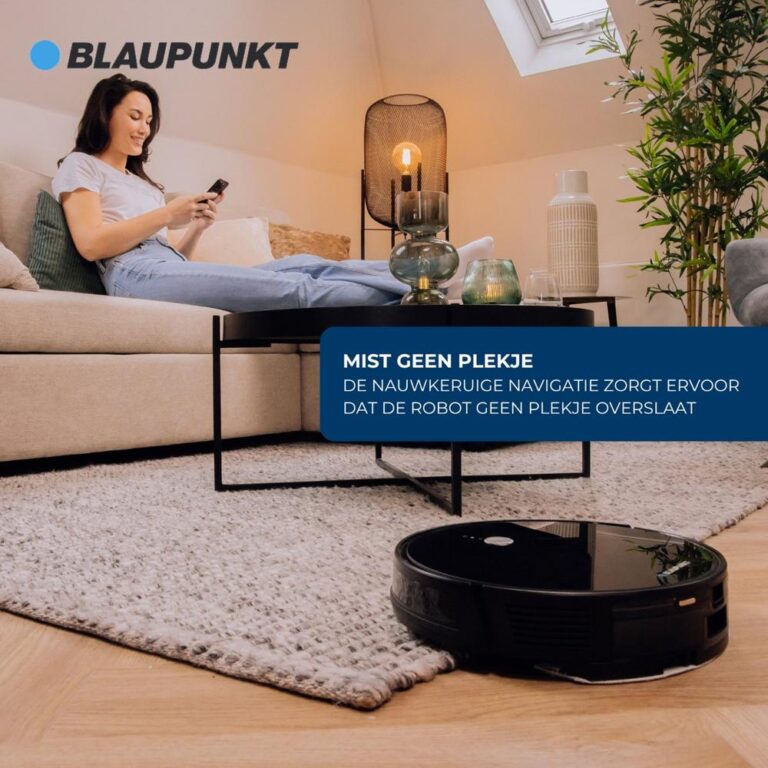 Een vrouw zit ontspannen op een bank en kijkt naar haar smartphone, terwijl een robotstofzuiger op de vloer in de buurt aan het werk is. De ruimte heeft een moderne inrichting met een tapijt, een salontafel en een lamp, wat een gezellige sfeer creëert.