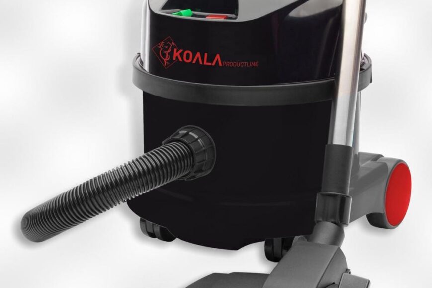 Een zwarte stofzuiger van het merk Koala met een ronde vorm en een handvat bovenop. De slang is ontworpen om flexibiliteit te bieden, terwijl de zuigmond op de grond staat, klaar voor gebruik.