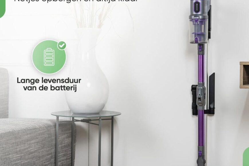 Een draadloze stofzuiger staat rechtop tegen de muur, naast een klein ronde bijzettafeltje met een witte vaas. De afbeelding benadrukt het opberg- en oplaadgemak en de lange levensduur van de batterij.