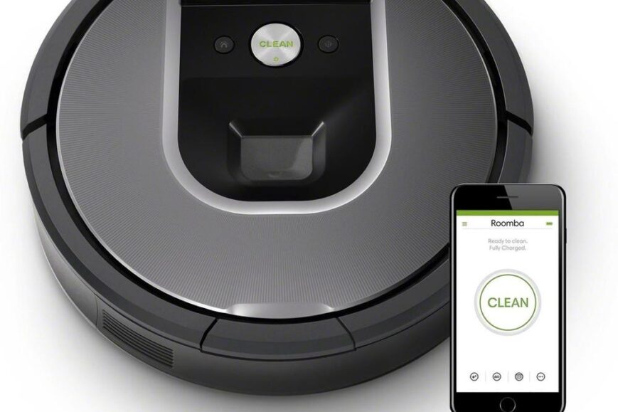 Een iRobot Roomba stofzuiger is afgebeeld met een smartphone ernaast die de app toont. De stofzuiger is rond en heeft een modern design, met een duidelijk zichtbaar ‘CLEAN’ knop op de bovenkant.