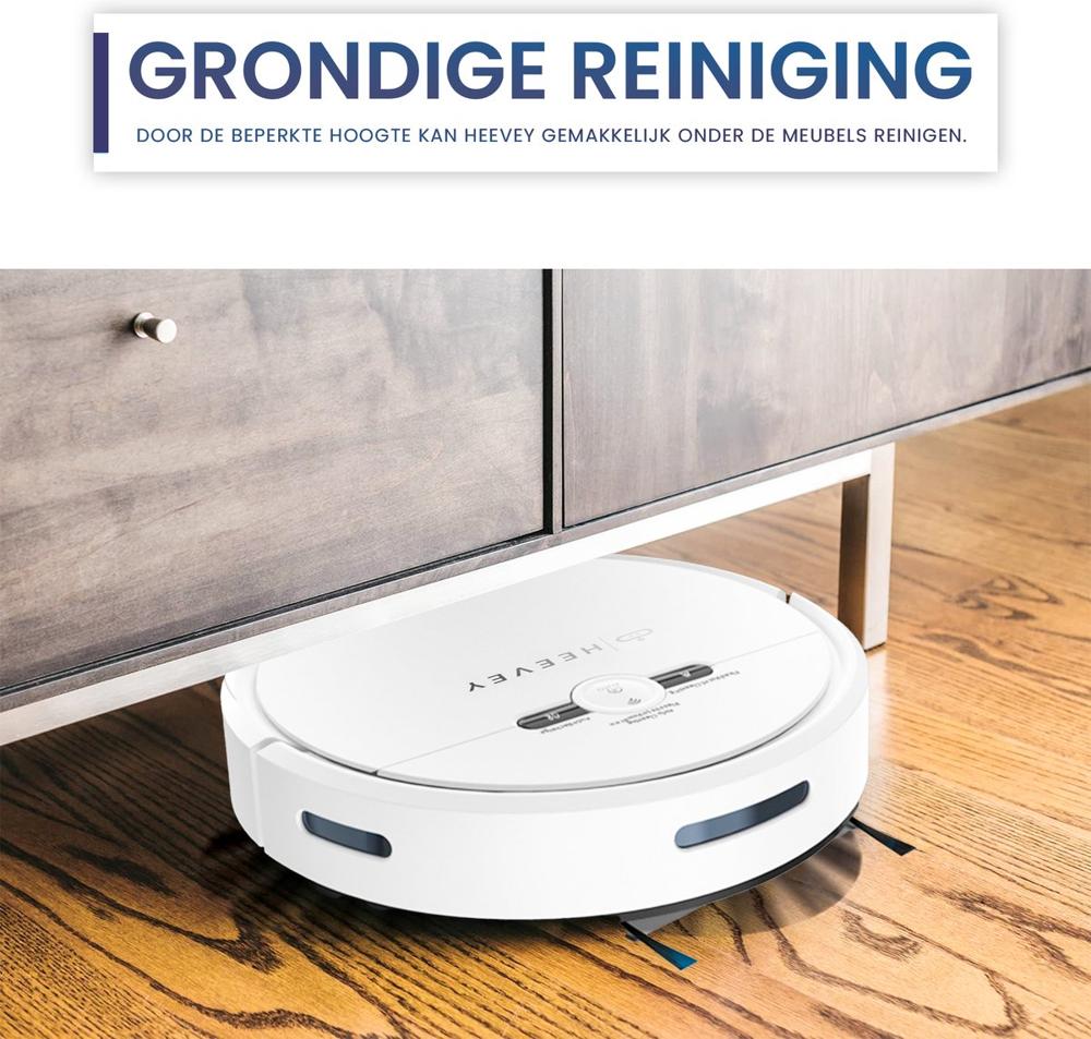 Een witte robotstofzuiger bevindt zich onder een laag meubelstuk op een houten vloer. Boven de stofzuiger staat de tekst "Grondige reiniging" die de functionaliteit benadrukt van het apparaat dat moeilijk bereikbare plekken kan schoonmaken.