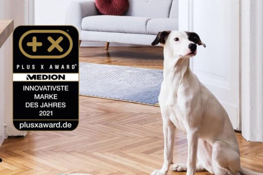 Een witte robotstofzuiger staat op een houten vloer terwijl een hond nieuwsgierig kijkt. Boven de afbeelding staat een tekst die aangeeft dat het product geschikt is voor allergische personen, met een Plus X Award-label dat de innovatie benadrukt.