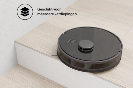Een zwart robotstofzuiger staat op de rand van een trap, uitgerust met een anti-valsensor die voorkomt dat hij van de trap valt. De achtergrond toont een houten vloer en een lichte muur, terwijl de stofzuiger klaar is voor gebruik op meerdere verdiepingen.