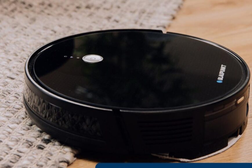 Zwarte robotstofzuiger van Blaupunkt staat op een houten vloer naast een gebreide mat. De afbeelding benadrukt de krachtige zuigkracht en de verschillende zuigstanden van het apparaat.