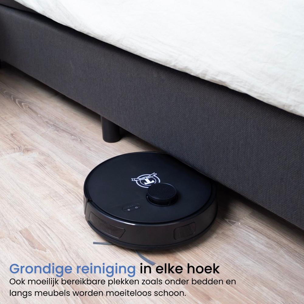 Een zwarte robotstofzuiger staat onder een bed en reinigt de vloer. De afbeelding benadrukt de effectiviteit van het apparaat in moeilijk bereikbare hoeken en onder meubelen.