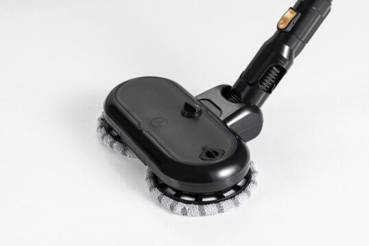 Een schoonmaakapparaat met een zwarte behuizing en twee ronde, grijze microfiber pads. Het apparaat is ontworpen voor het effectief reinigen van verschillende oppervlakken en heeft een ergonomische handgreep voor gebruiksgemak.