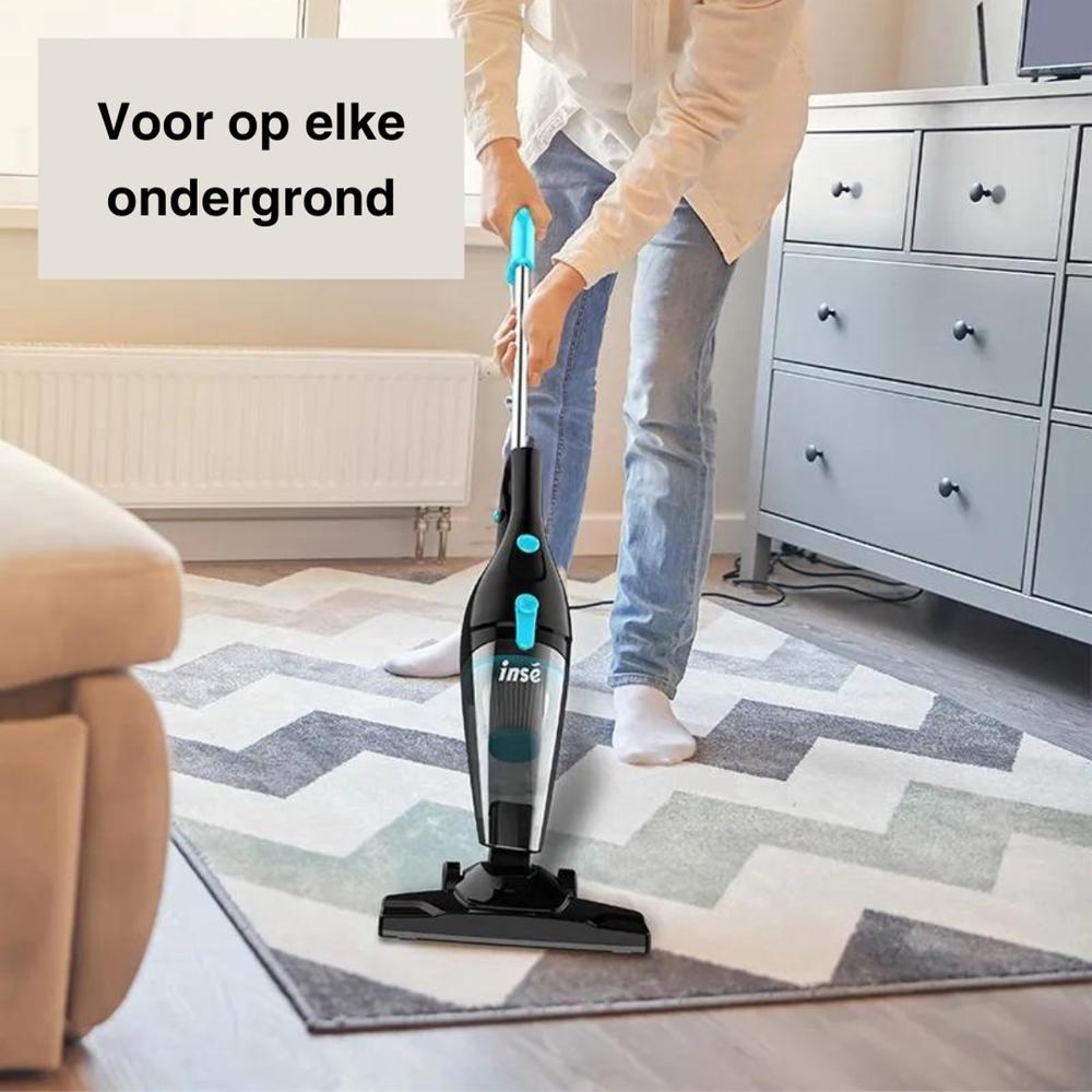 Een vrouw staat op een tapijt en gebruikt een handstofzuiger. De stofzuiger is zwart met blauwe accenten en is ontworpen voor gebruik op verschillende ondergronden.
